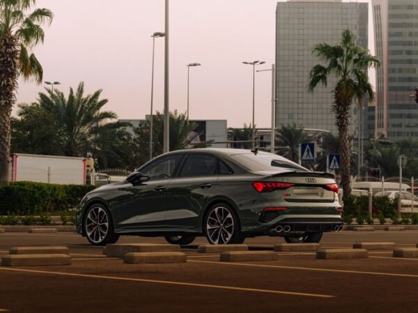 Stylish luxury car parked in a modern cityscape with palm trees at sunset.