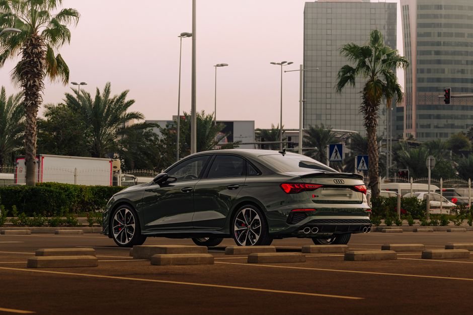 Stylish luxury car parked in a modern cityscape with palm trees at sunset.